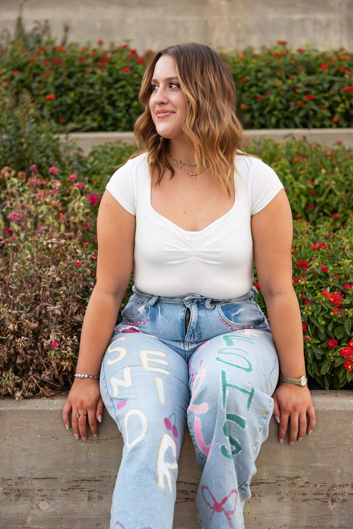 Senior girl in white top sitting on the edge of a garden during golden hour in Lawrence KS