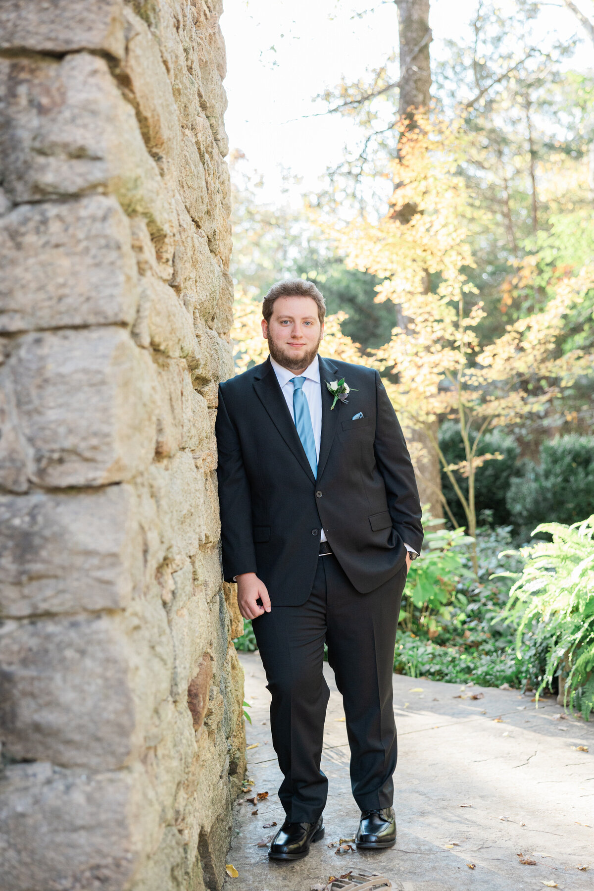 A man in a suit leaning against a stone wall