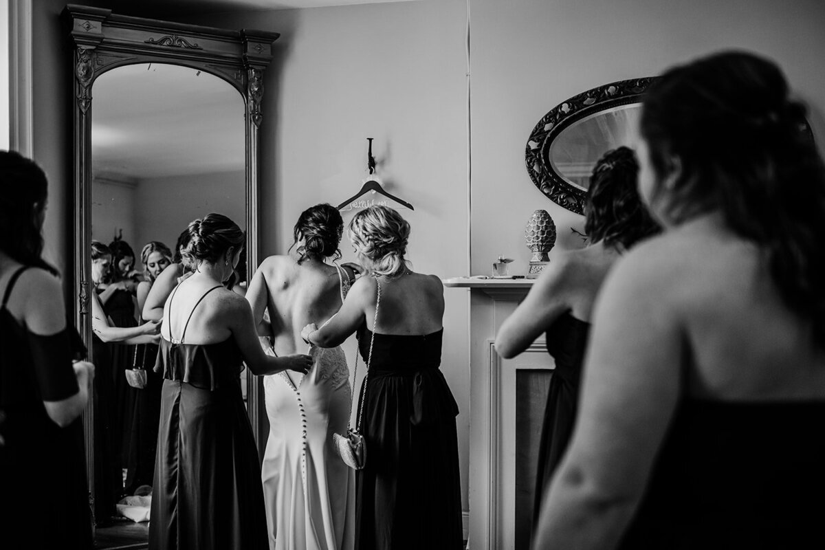Black and white wedding photo of bride getting into her wedding gown with the help of her bridesmaids in her bridal suite captured by Maryland wedding photographer