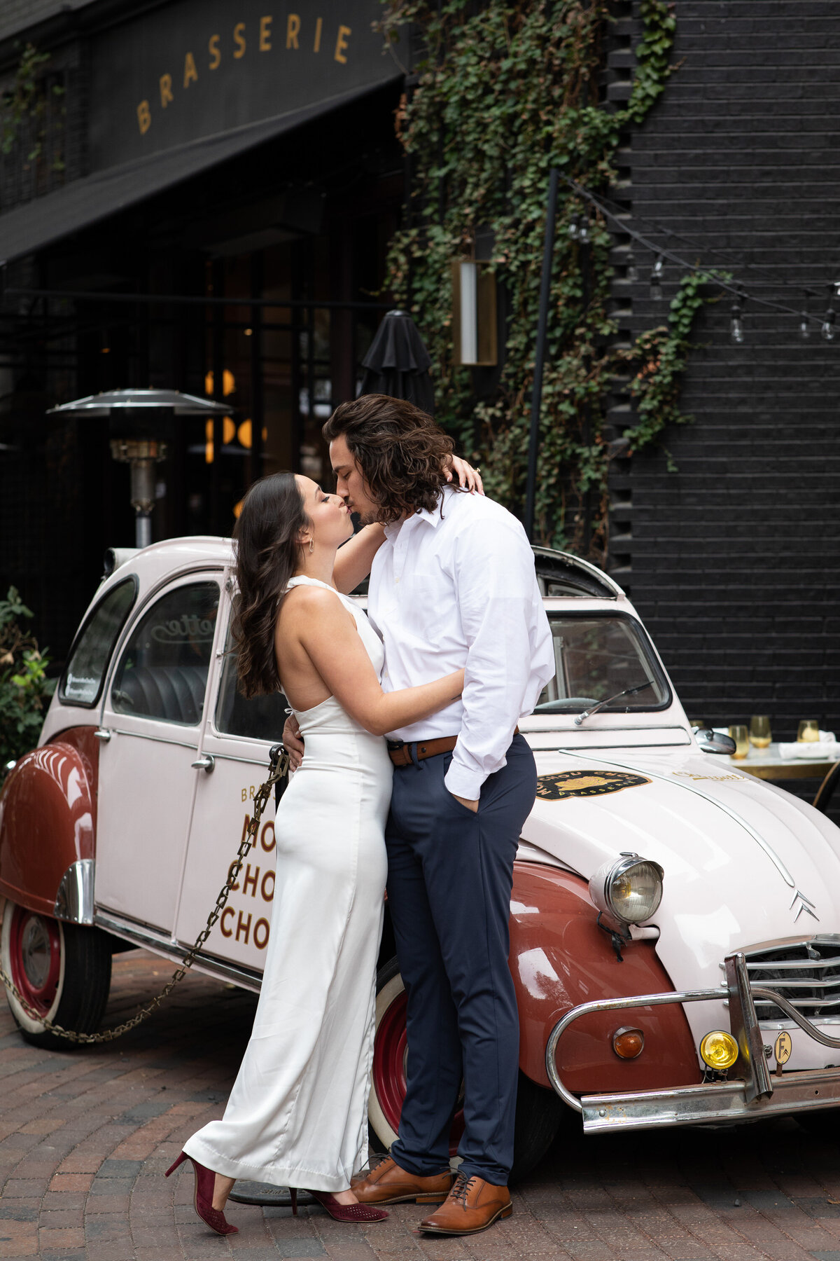 A bride and groom kiss in front of a vintage car captured by an Austin wedding photographer.