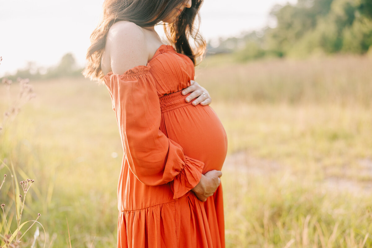 Close up of expecting mom's baby bump while wearing an orange dress.