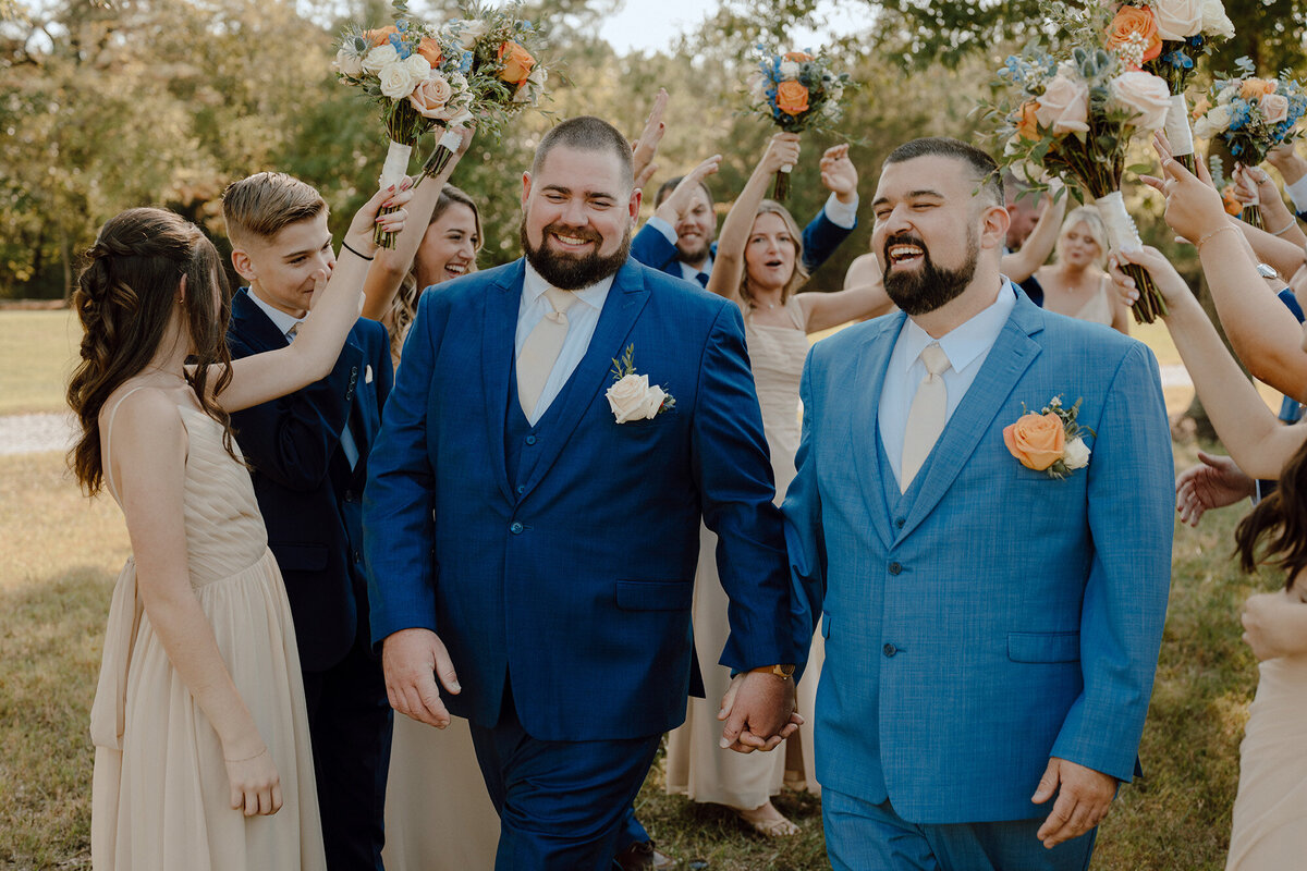Two grooms holding hands walking down the aisle 
