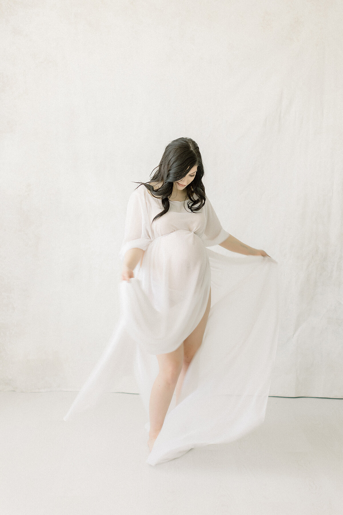 A photo taken for a maternity session in a Dallas/Fort Worth area photography studio of an expecting mother while she is dancing playfully around the studio.