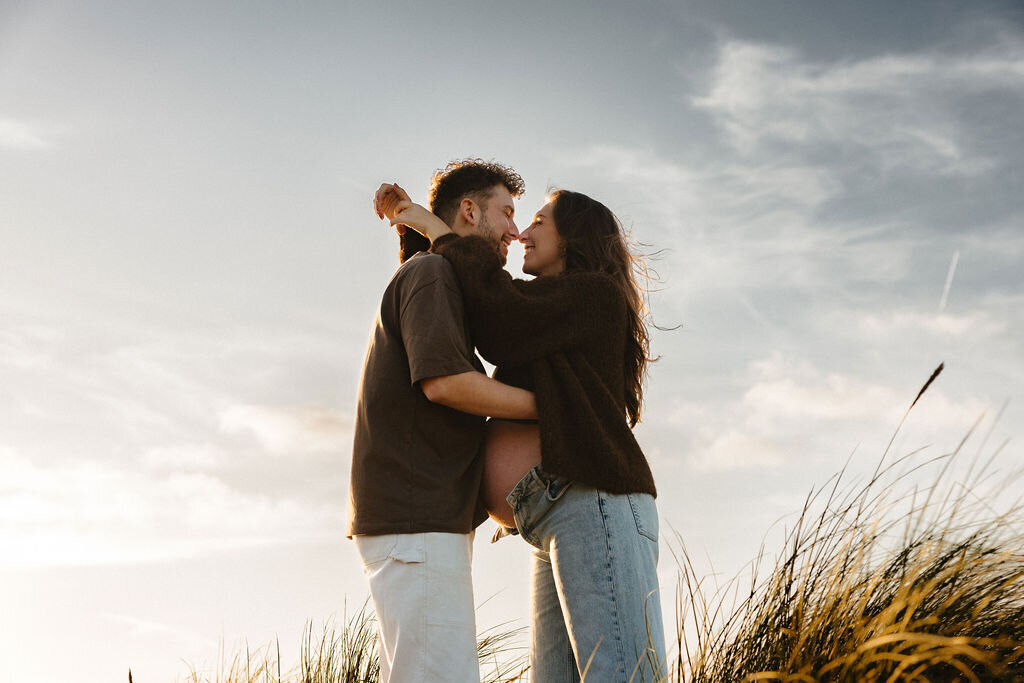 Koppel omhelst elkaar tijdens golden hour shoot zwangerschap op het strand