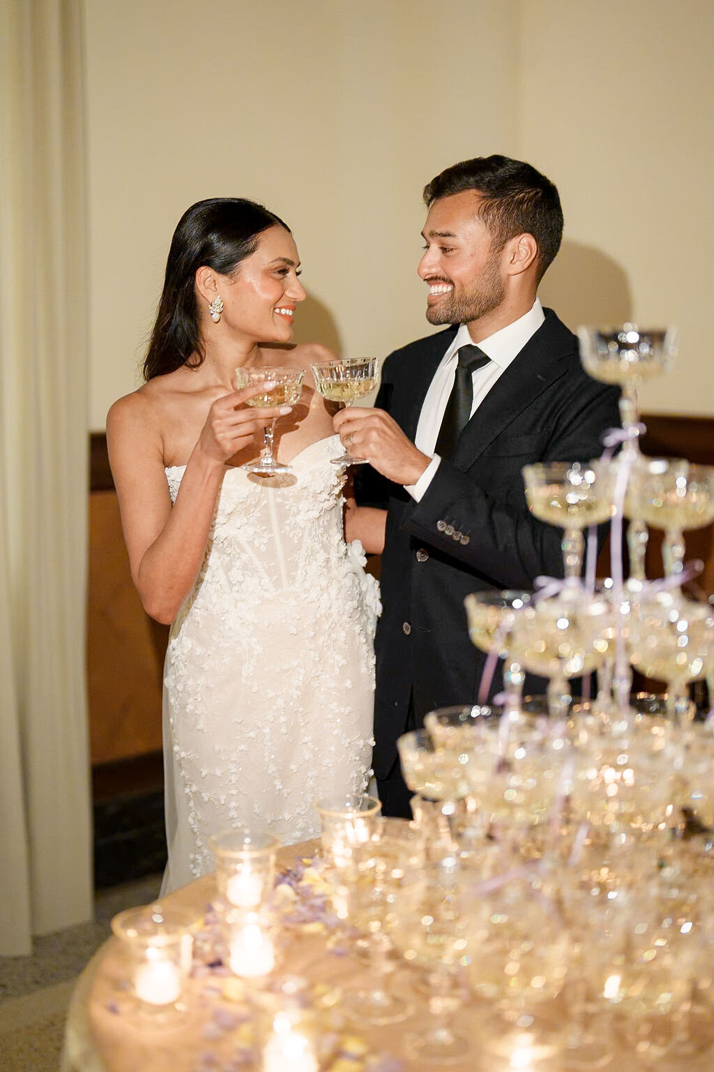 bride and groom smiling at each other at a champagne tower