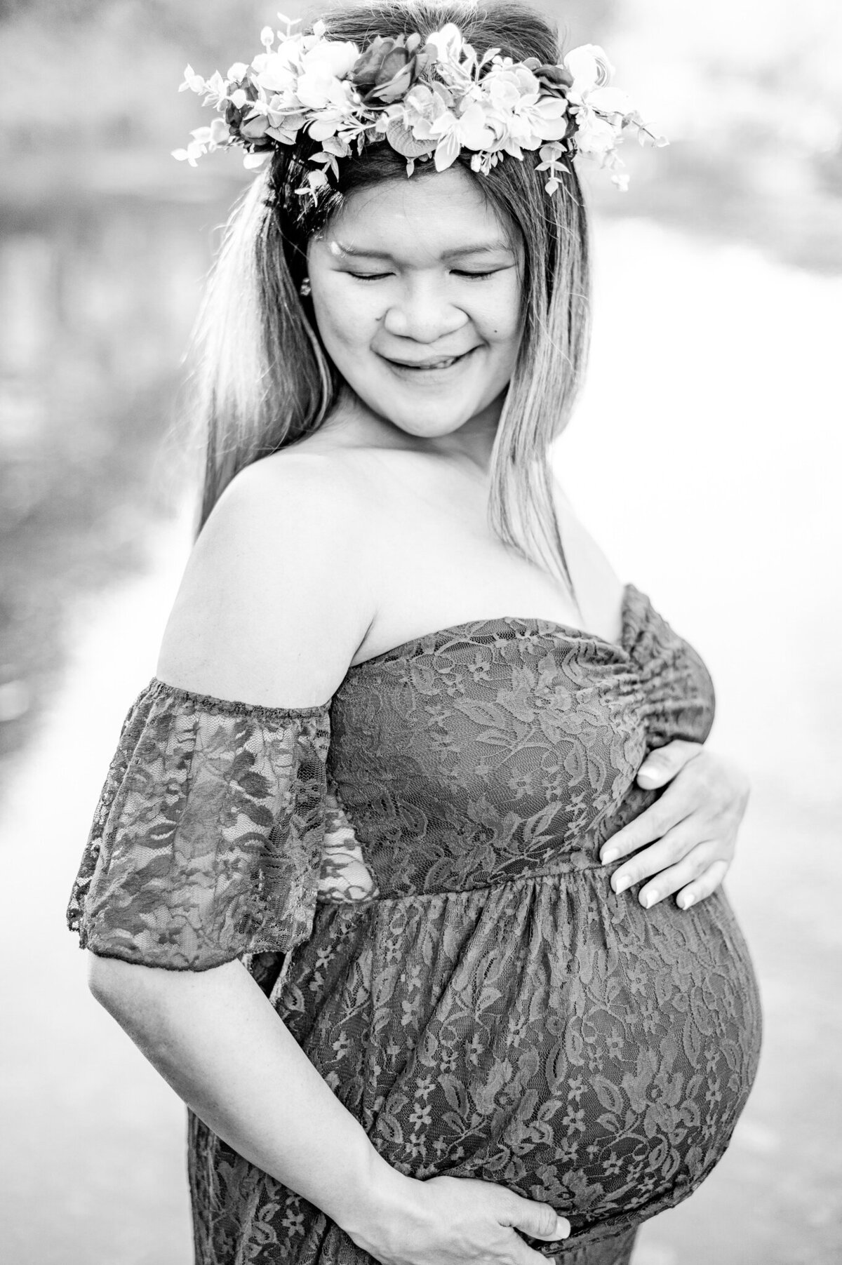 Black and white image of a pregnant woman holding her bump and smiling down over her shoulder during San Antonio maternity photos.