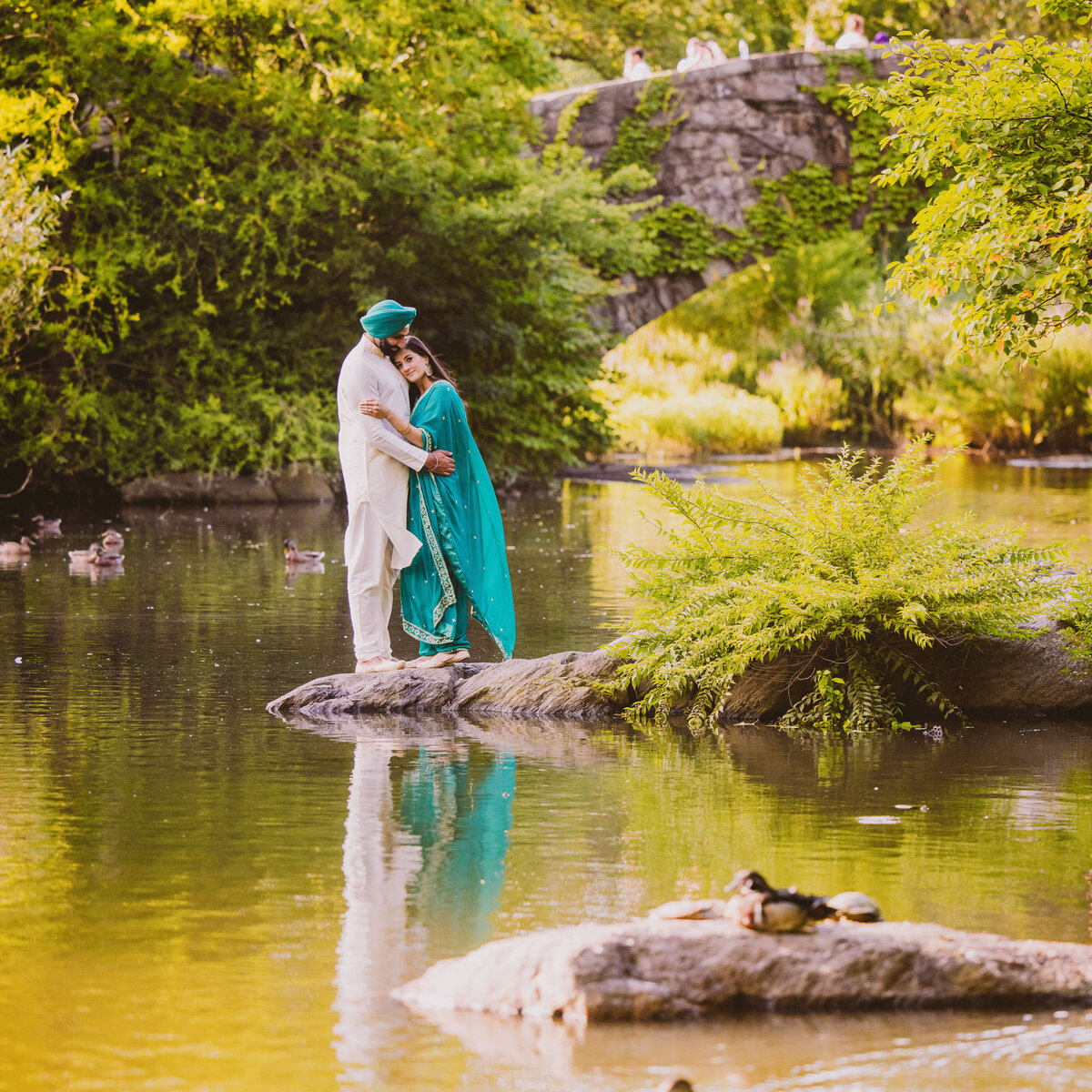 Engagement couple in punjabi indian outfits standing near the central park pond with the gapstow bridge in the background