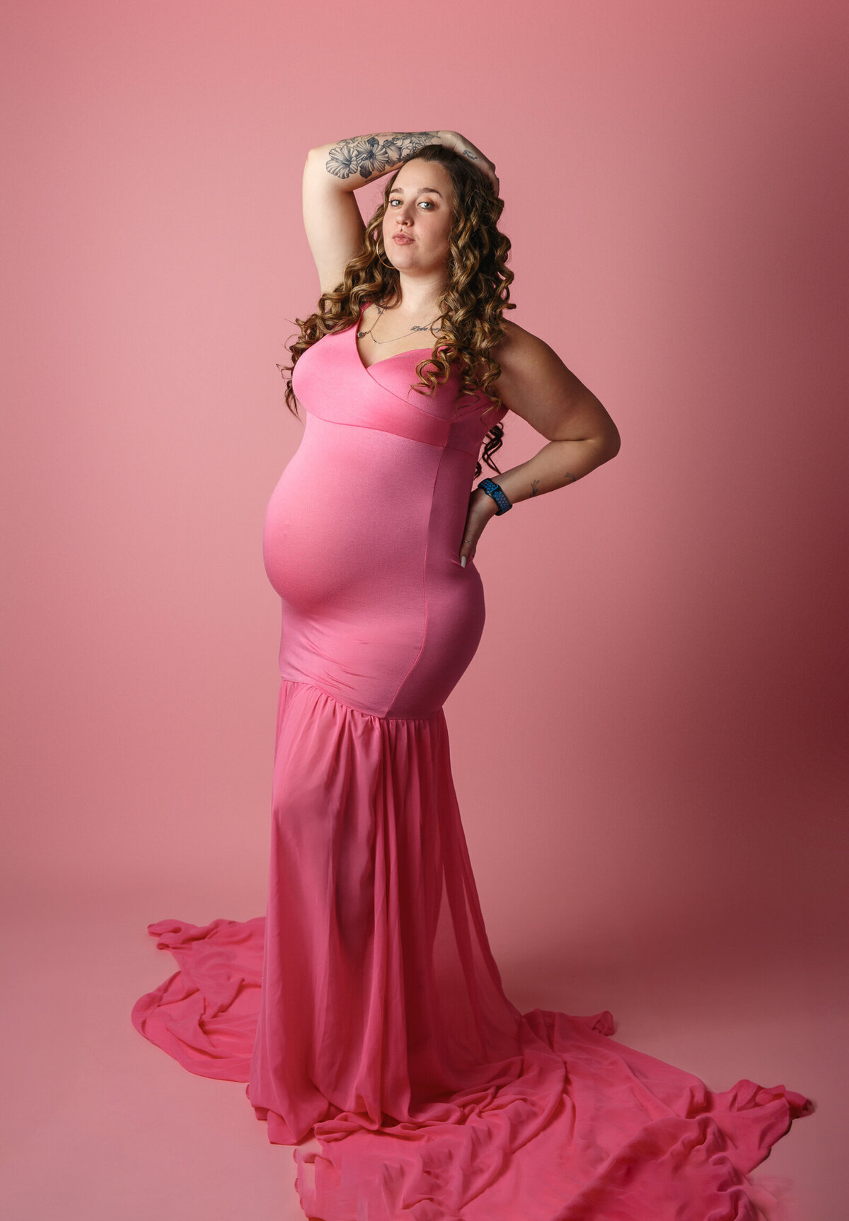 Pretty pregnant woman wearing a pink gown and photographed on a pink background