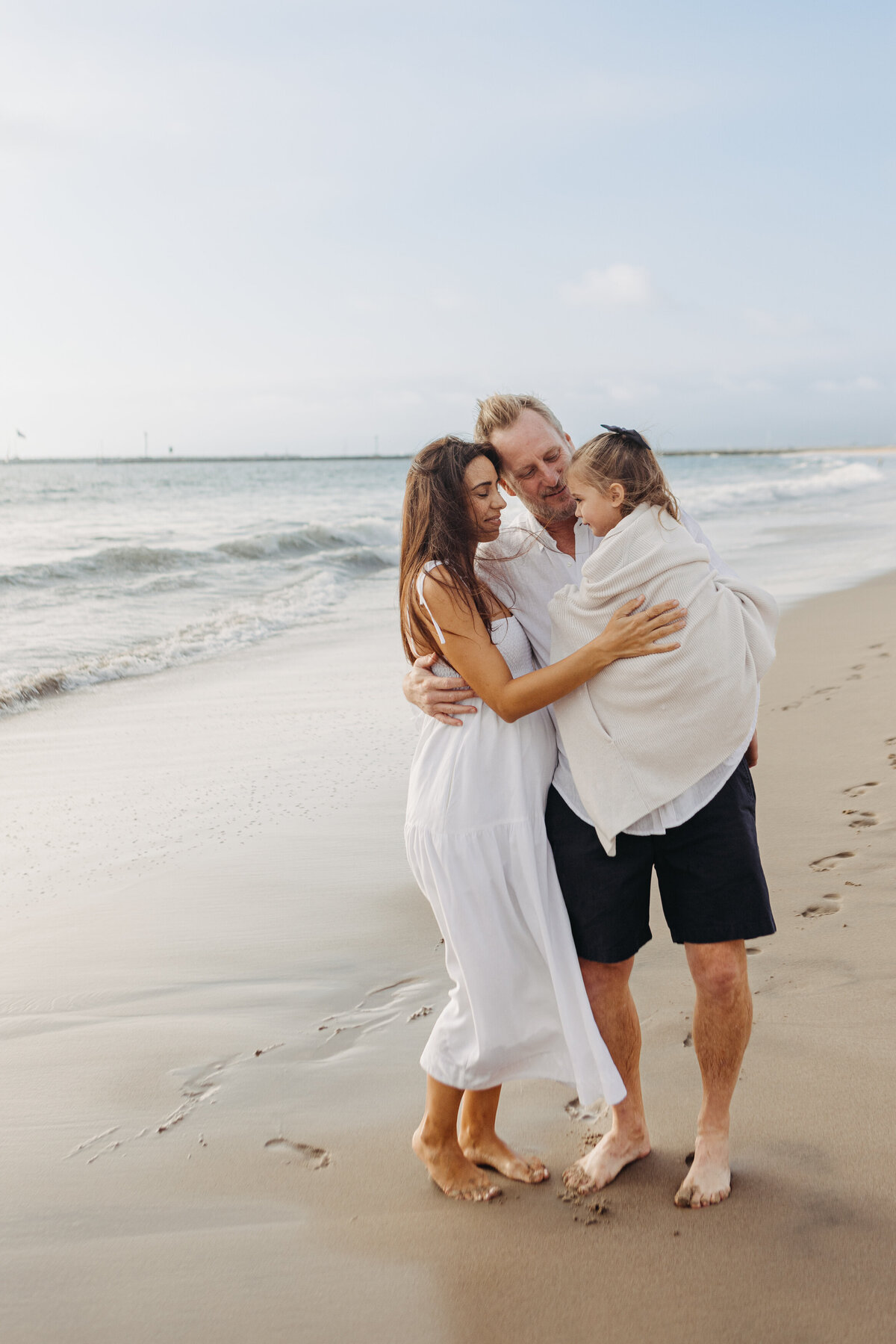 Family snuggles on the beach wearing white.