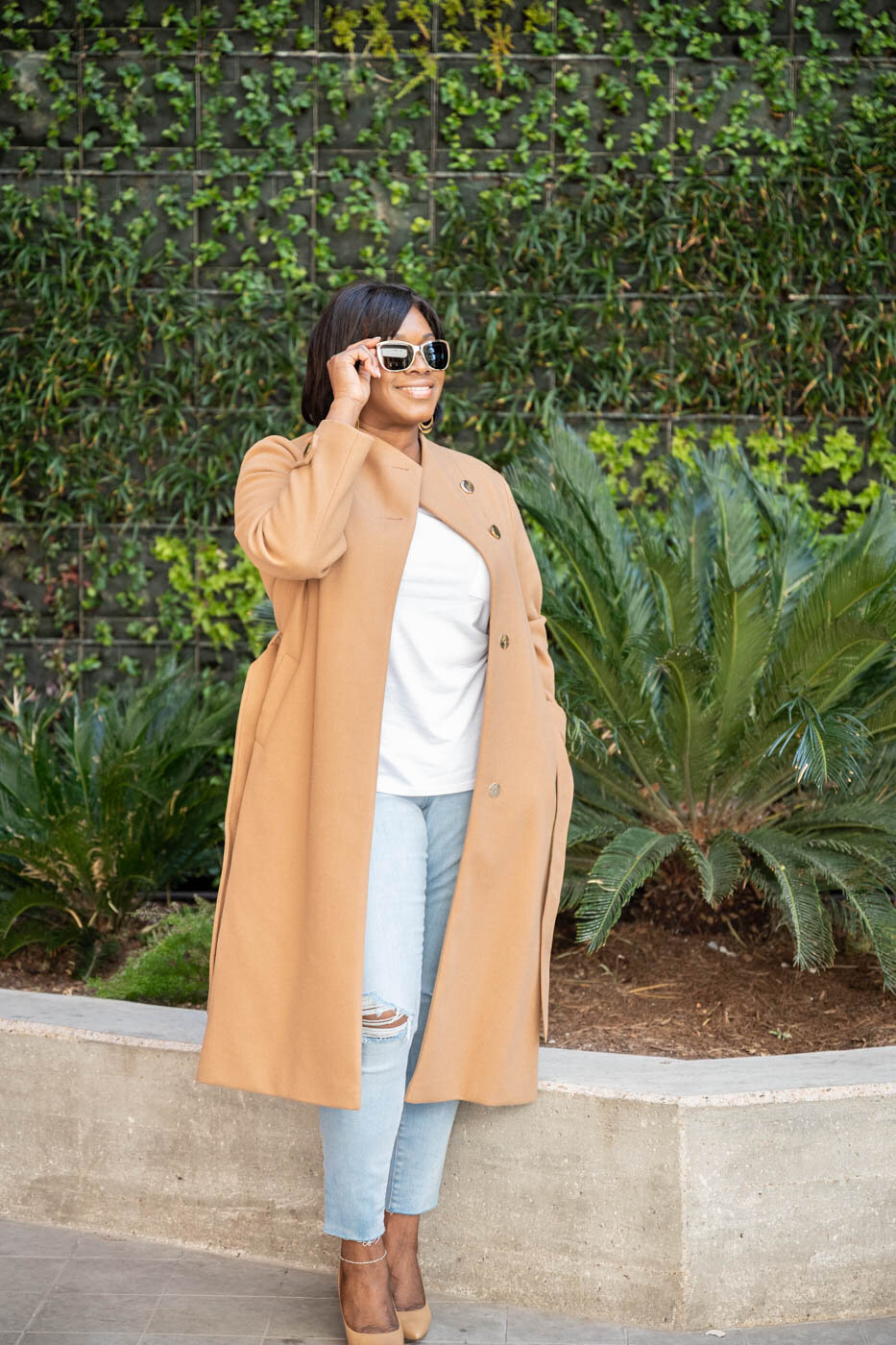 A portrait of a professional woman wearing a beige long coat and jeans with heels