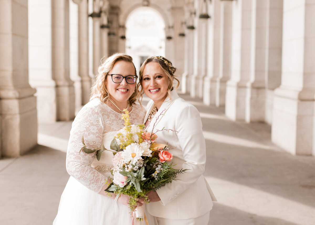Two brides stand side by side in front of pillars