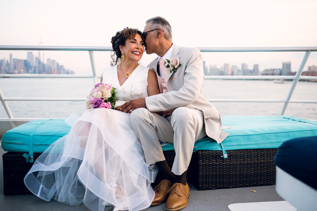 A bride and groom kiss on the deck of a boat.