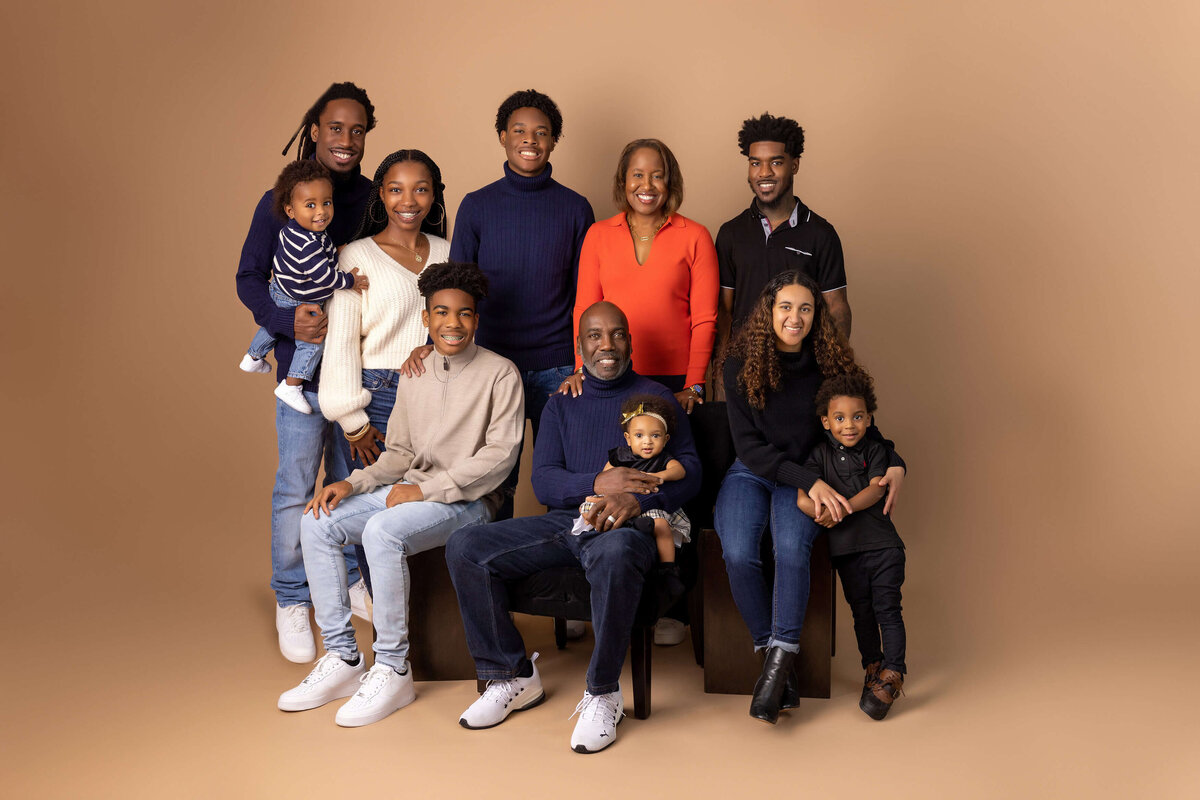 A three generation family portrait with eleven people. Three adults are seated in the front row holding two toddlers. Four adults and two children stand in the back row. Everyone is smiling, dressed in casual clothing, and posed against a plain beige background, capturing timeless Jacksonville family photography.