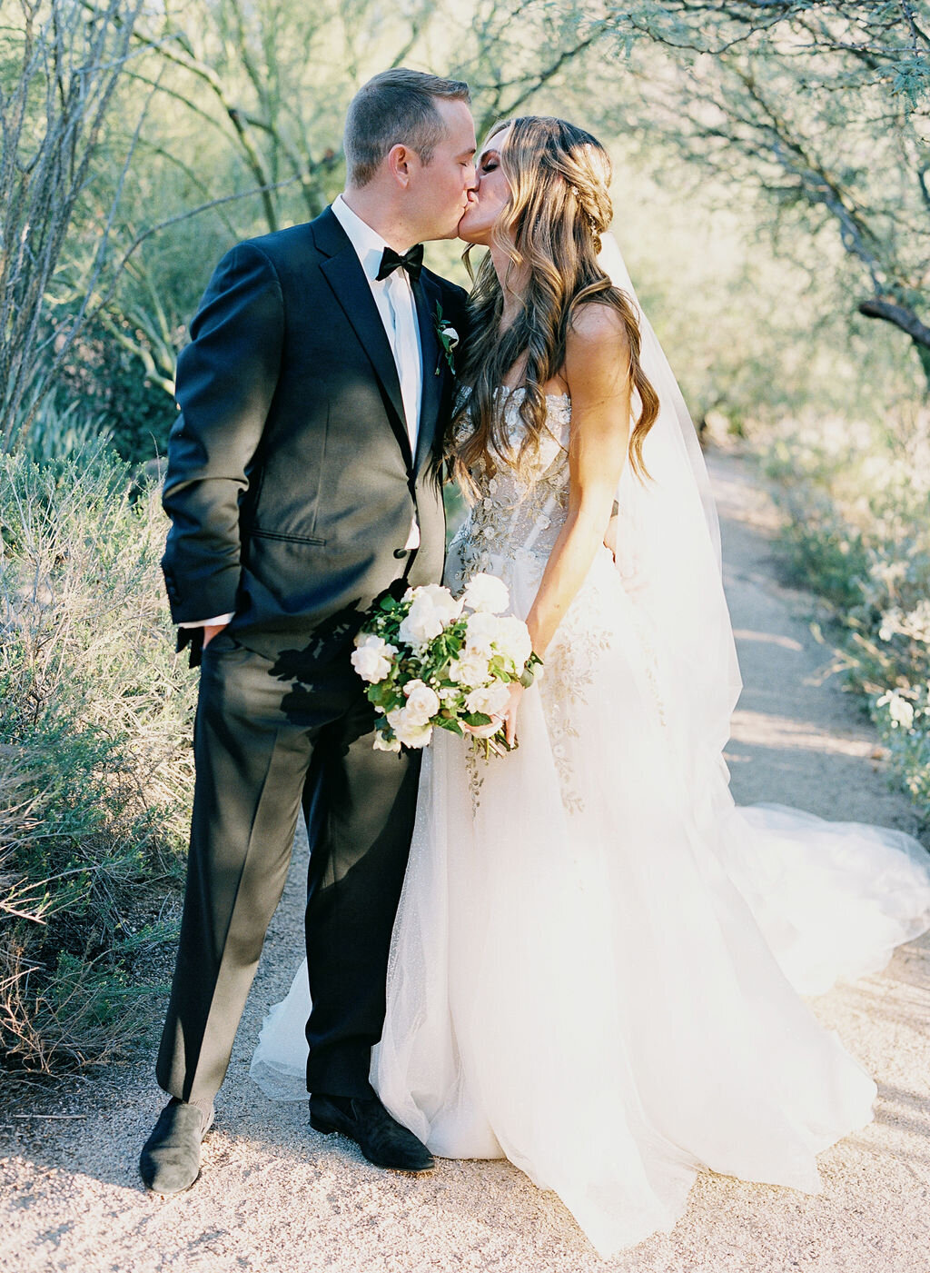 A stunning wedding portrait of the bride and groom sharing a kiss in a breathtaking desert landscape, capturing timeless love.