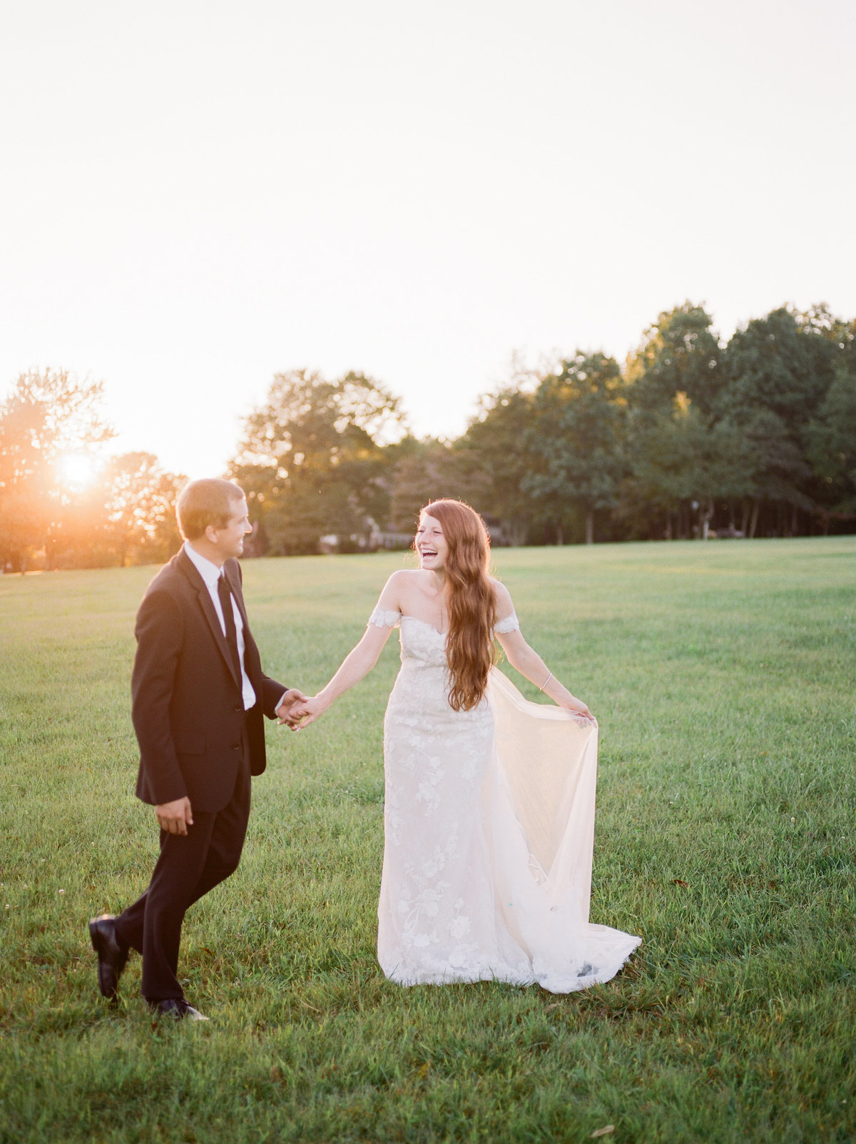 bride and groom walking through grassy field holding hands