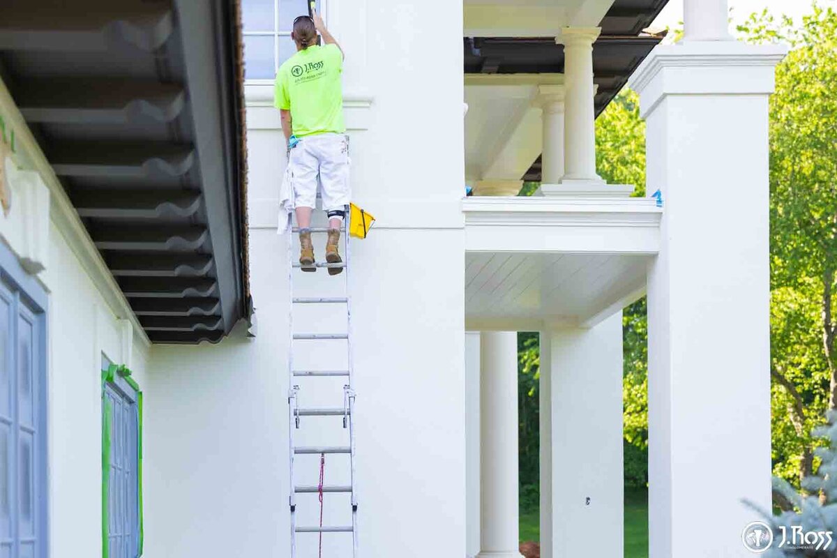 Close-up of a painter on a tall ladder applying final coats to the upper trim and eaves of the portico, highlighting precision home exterior painting Bristol, VA at height.