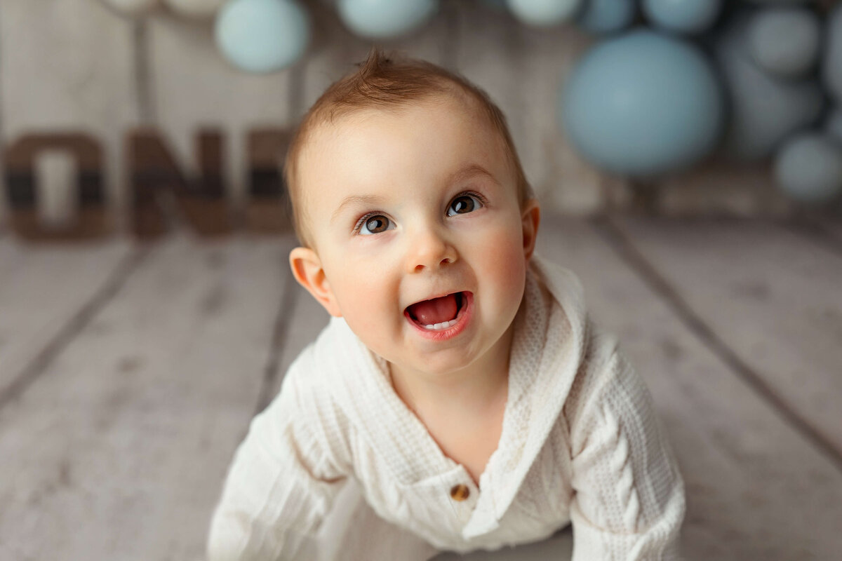 1 year old boy in white outfit at a one year cake smash session