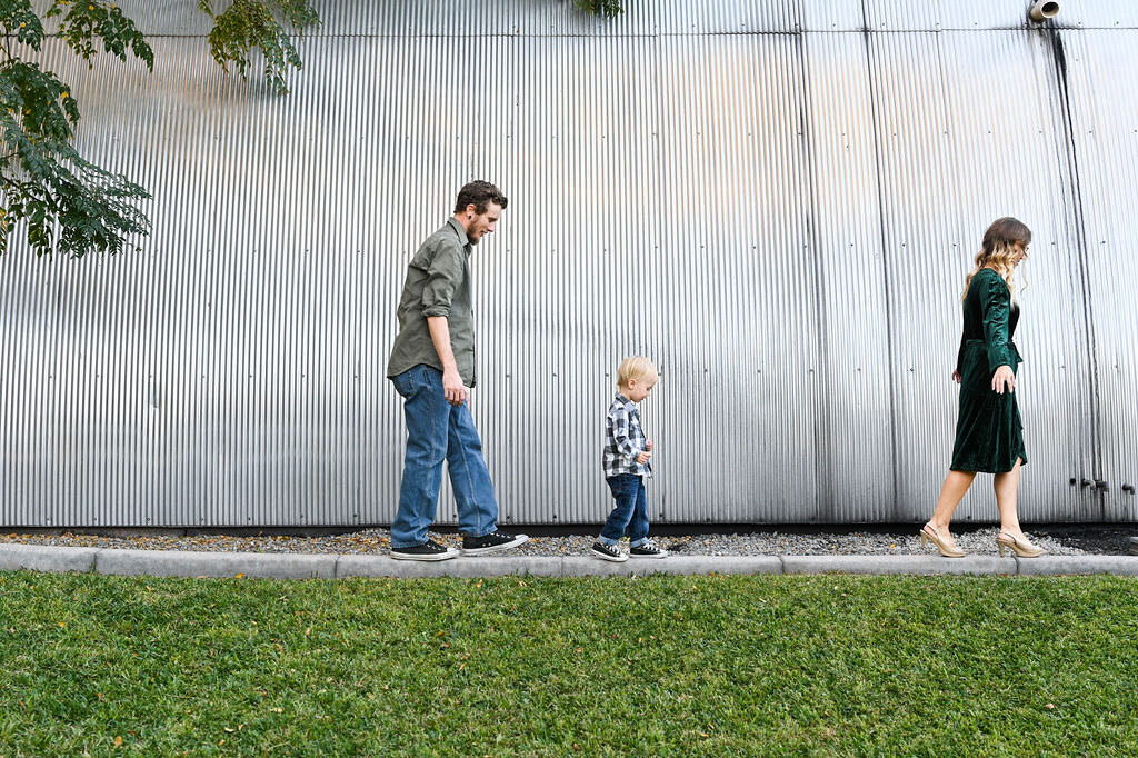 A small child walking in between their parents on a sidewalk.