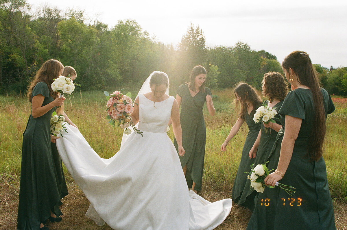 Bridesmaids adjusting a bride's dress during golden hour on film.