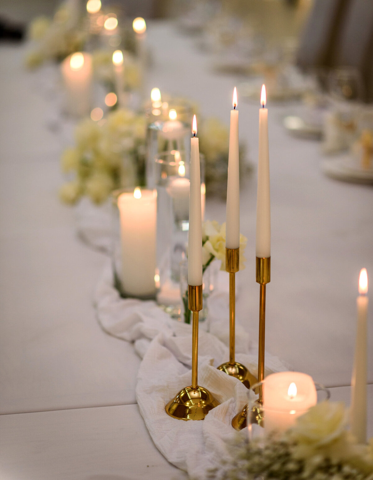 Elegant tablescape featuring gold taper candles and white pillar candles, creating a warm and romantic ambiance, designed by In Full Bloom Event Planning & Design.