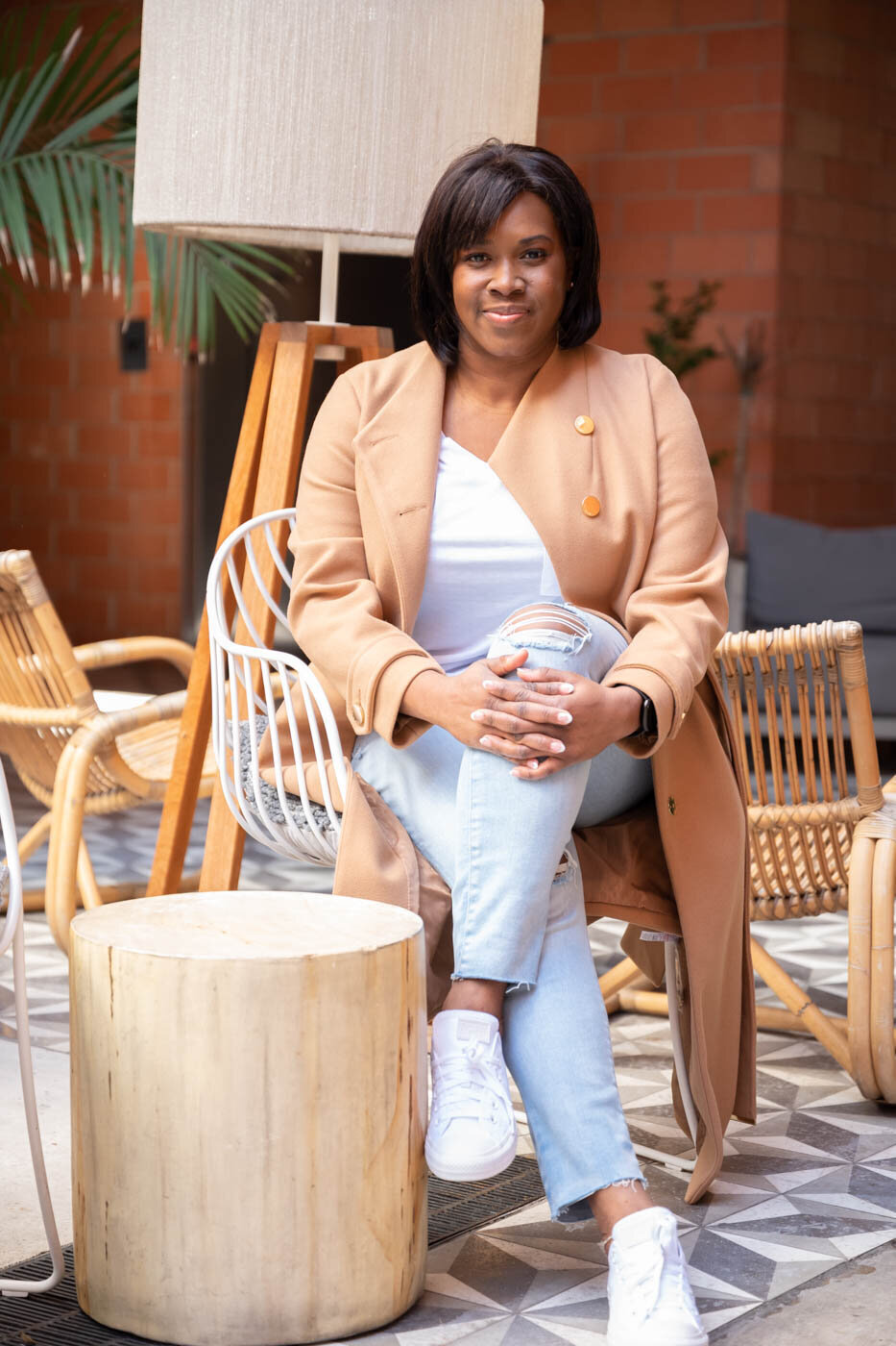 A portrait of a woman sitting outside of a restaurant wearing jeans and white tennis shoes