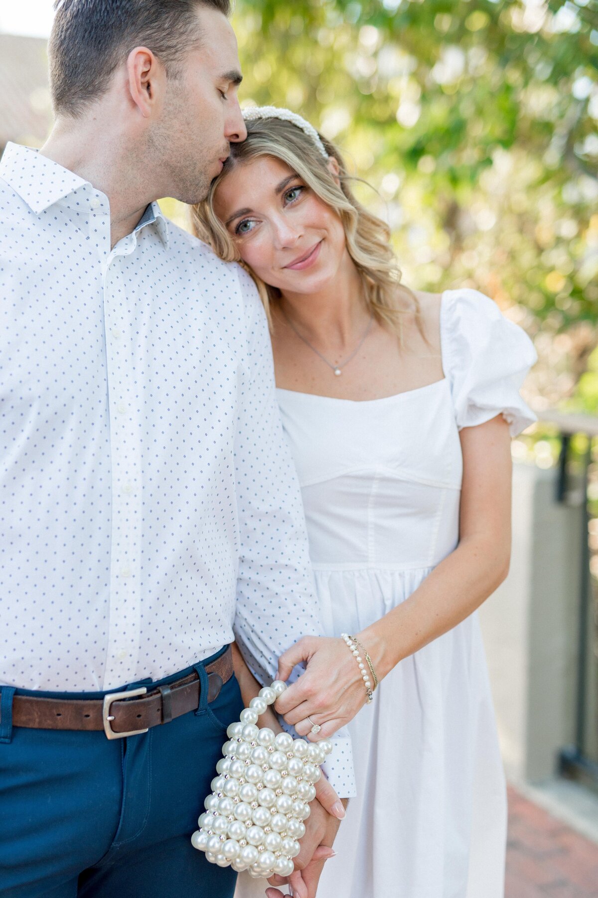 Sweet and sentimental engagement moment—bride-to-be leans into her groom with a soft smile and elegant, romantic style.