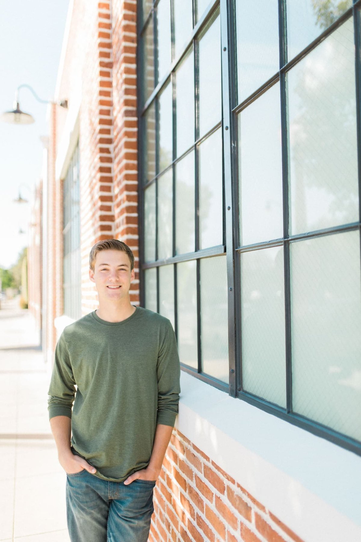 Young man poses for senior photos while leaning against a wall