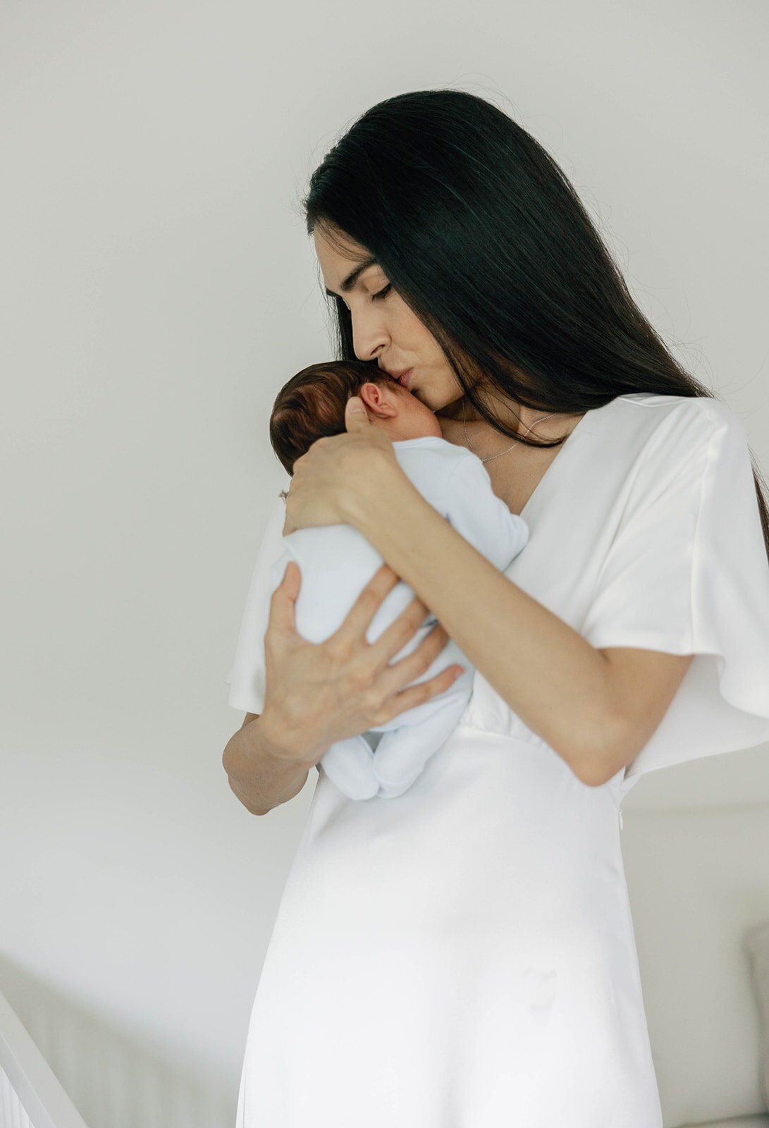  A mother dressed in white cradles her newborn in a serene home setting during a Florida Keys portrait photography session.