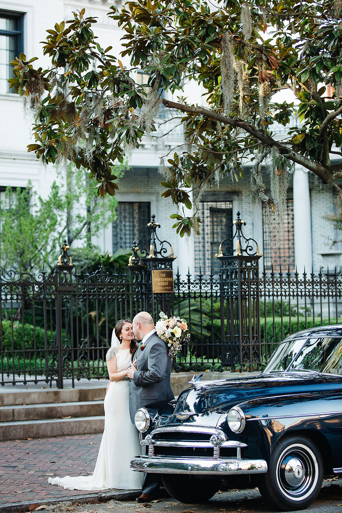 Bride and groom nuzzling one another beside car.