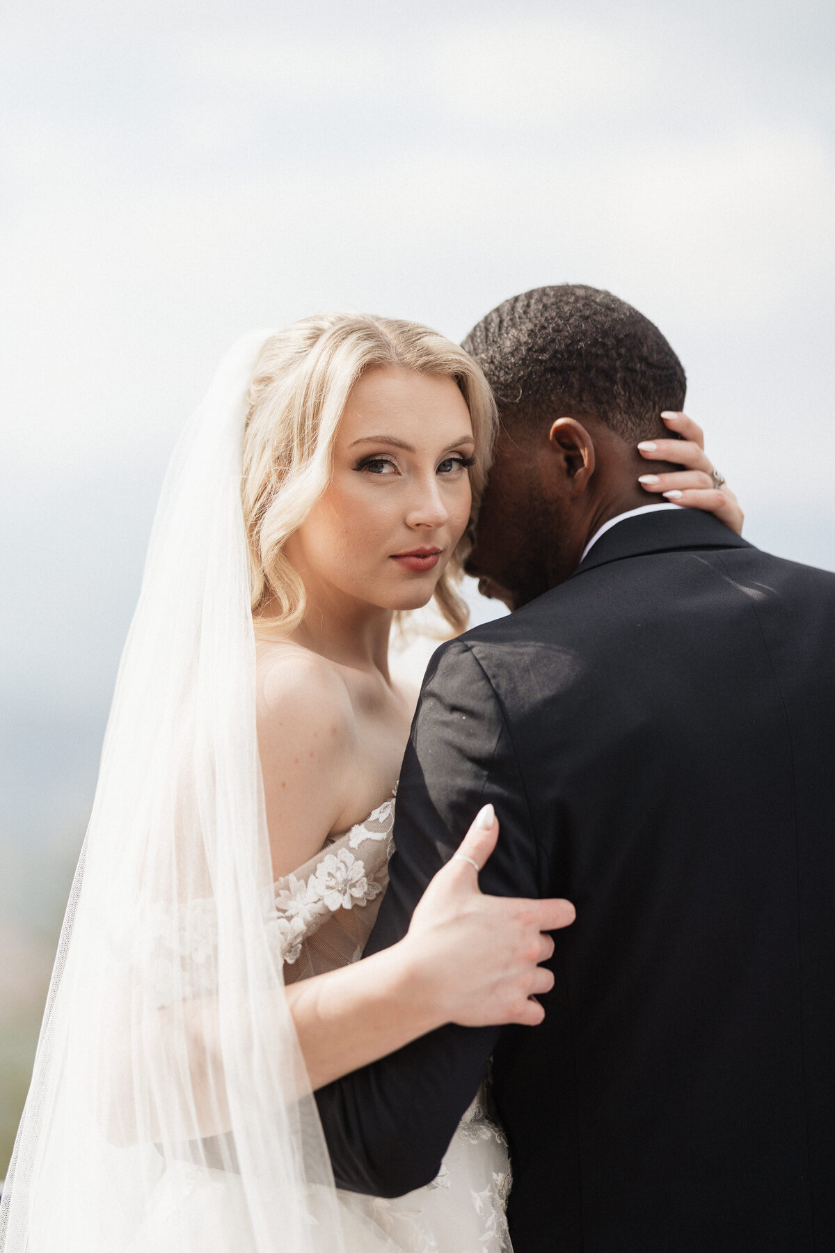 Bride looking into the camera as her groom is giving her a hug.