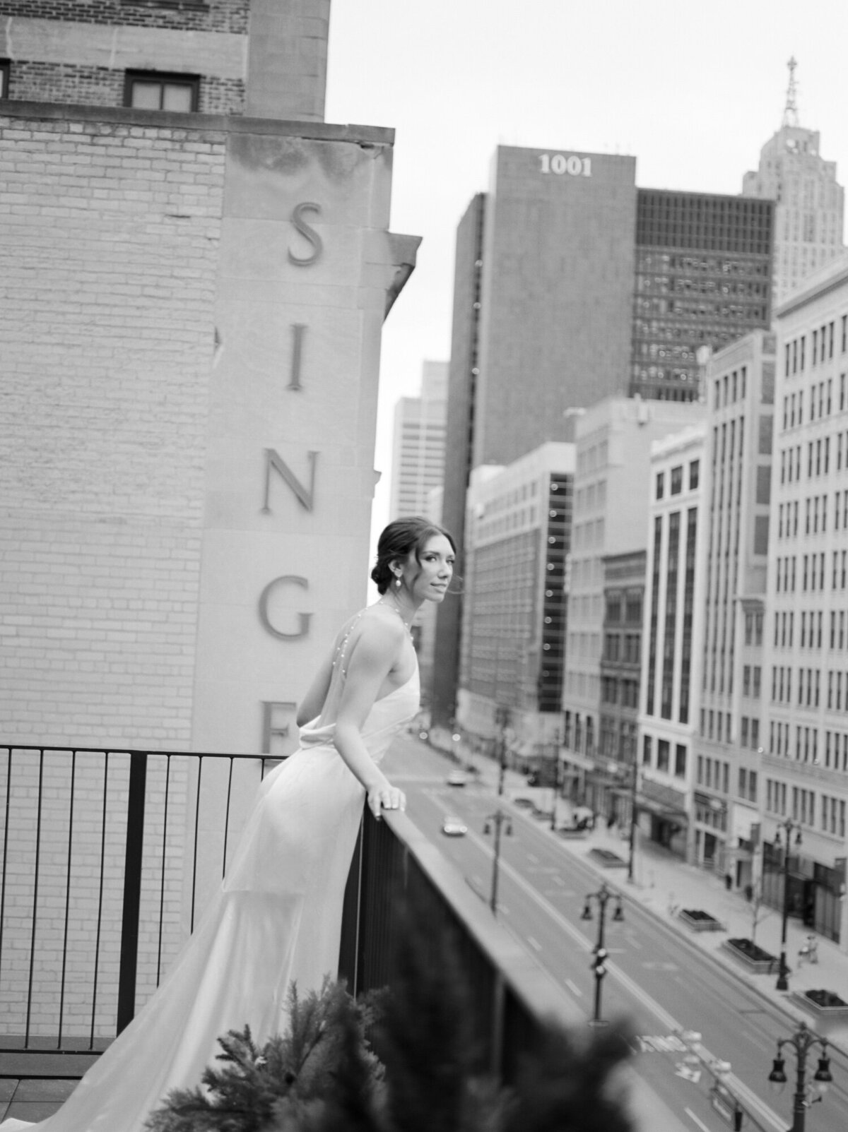 bride in backless wedding dress, pearl detail, leans over balcony of Detroit hotel