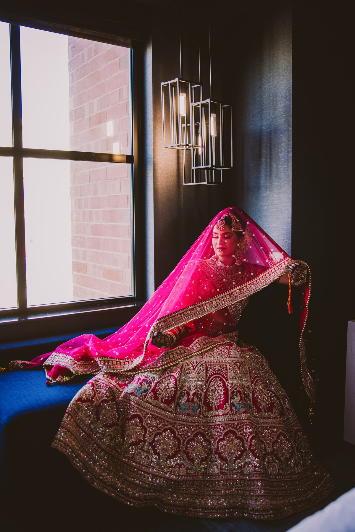 A sikh bride sitting in a hotel room on her wedding day with the red veil dupatta over her head at the marriott owing mills md