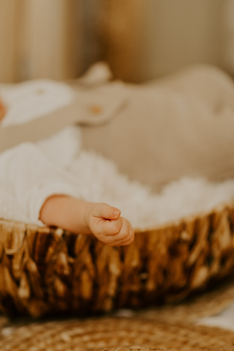 Zoom sur une petite main de bébé dépassant d'un panier en osier capturée par Laura, photographe naissance en Vendée.