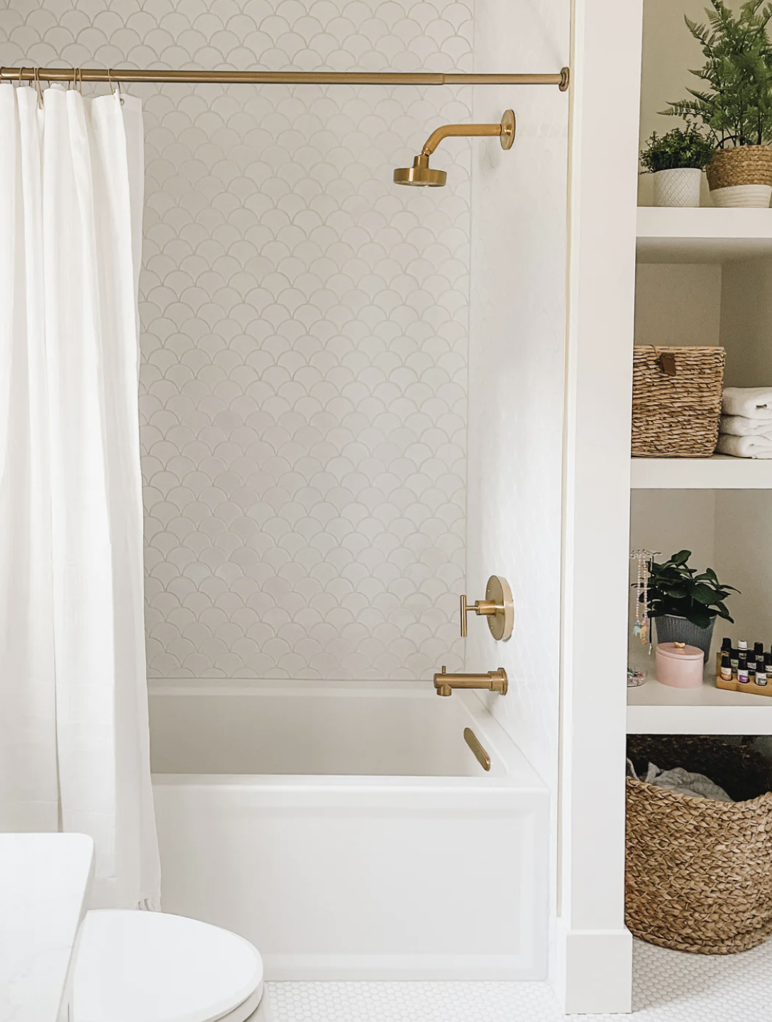 The upstairs guest bathroom features crisp white scalloped tile in the shower along with warm brass fixtures from Kohler