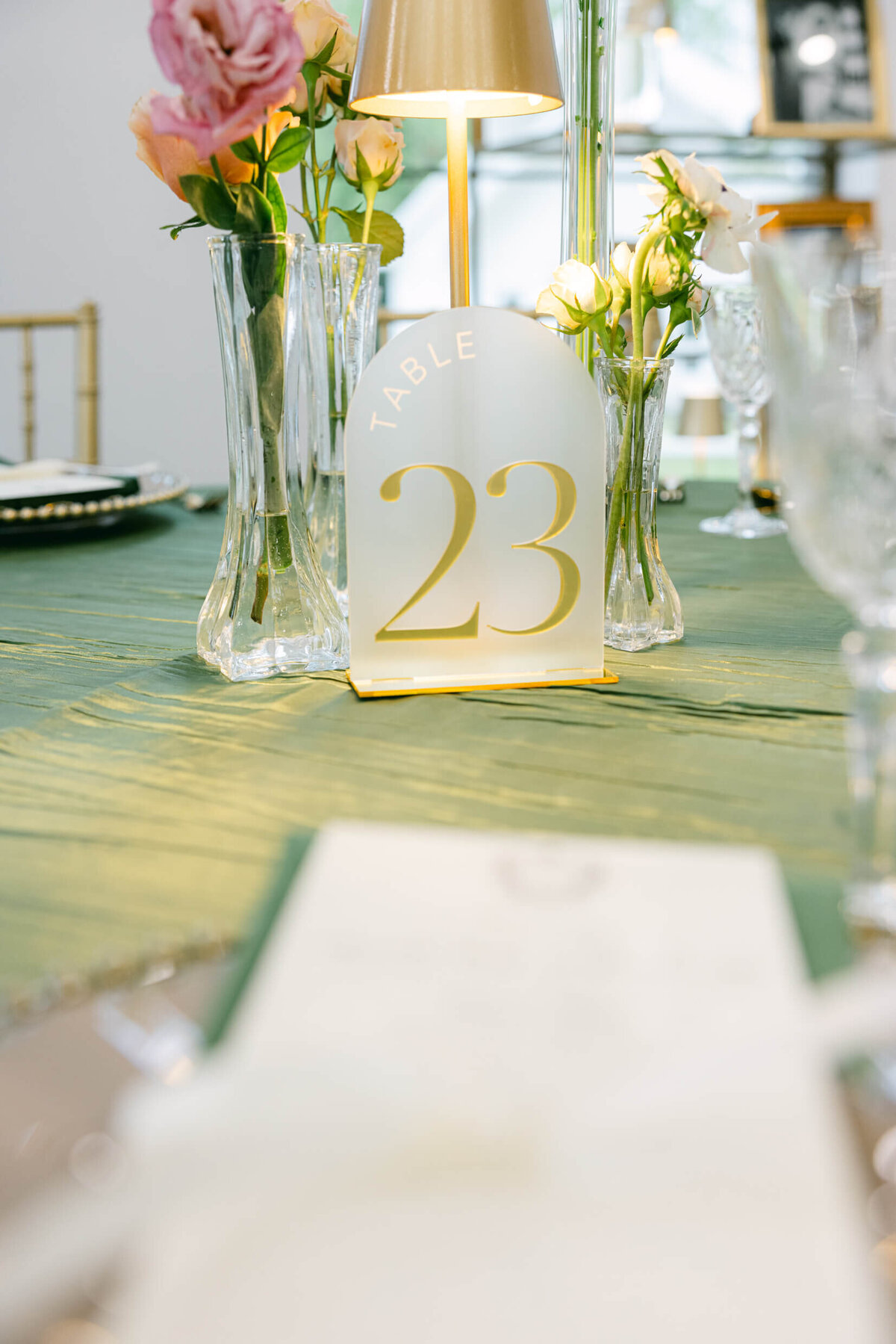 A wedding day photo of the tables in the reception hall that are covered in green linens with florals & candles on top
