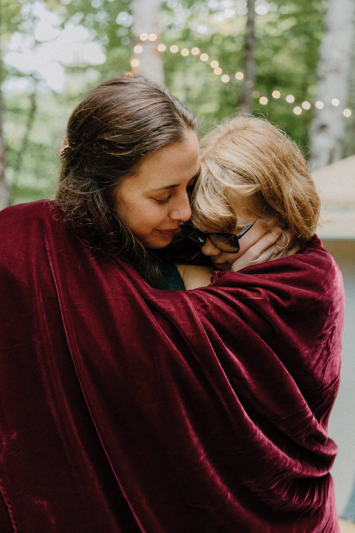 A mother and her child in a touching moment; hugging each other wrapped in a red blanket