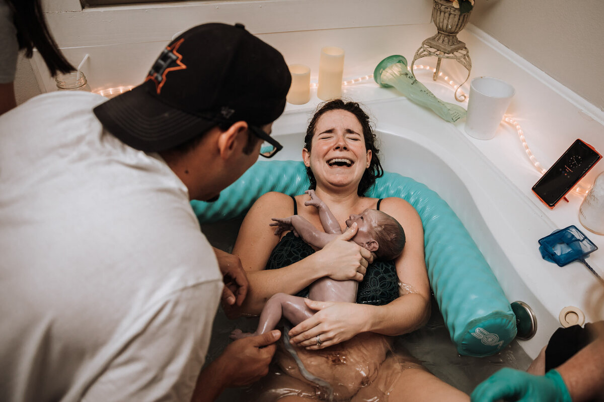woman in birth tub crying holding newborn