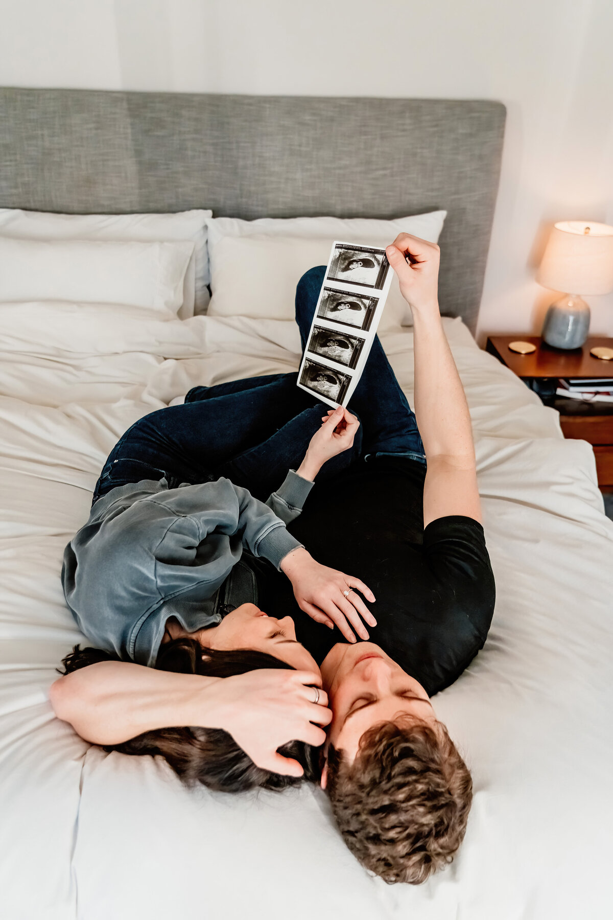 a couple looking at a sonogram of their baby, laying on their bed in their home photo shoot