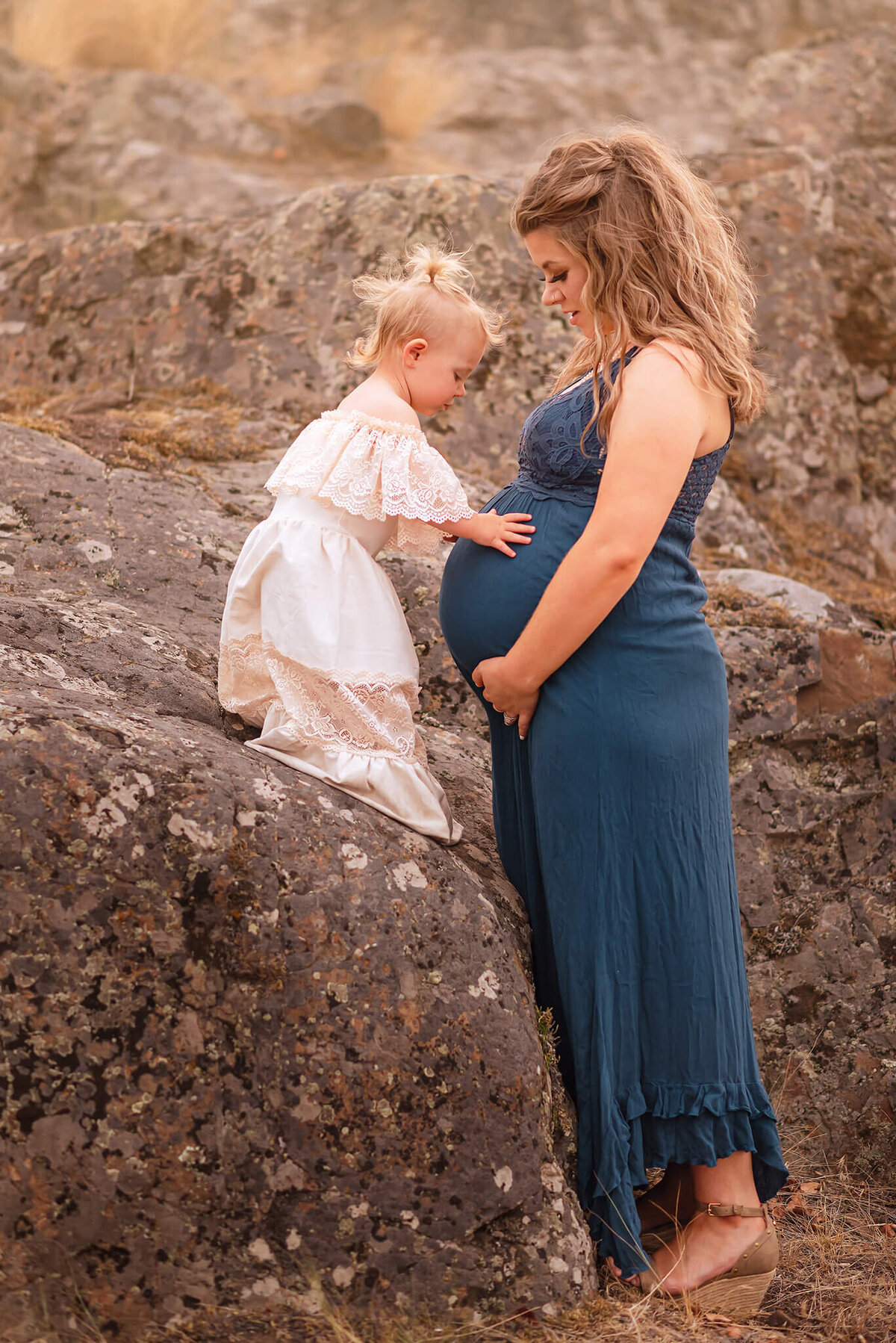 A pregnant woman stands while her toddler daughter embraces her belly. Taken in Kamloops