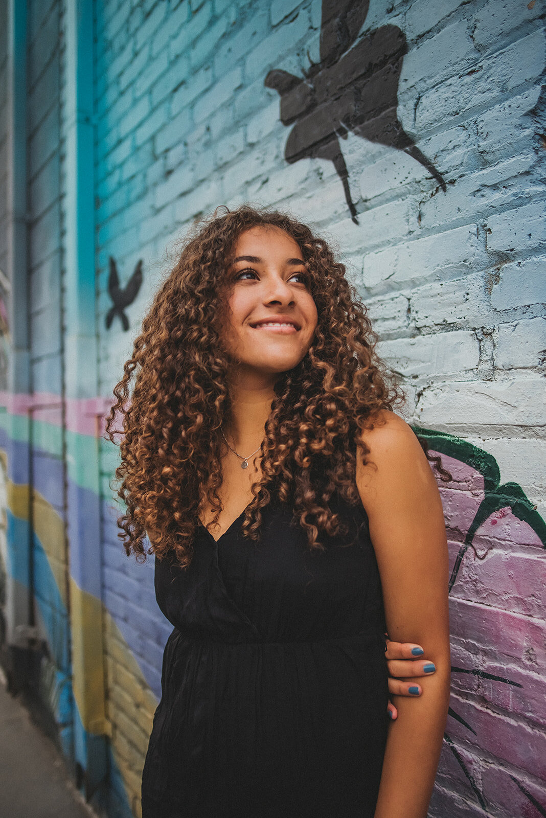 Girl smiles in front of a mural for senior headshots.