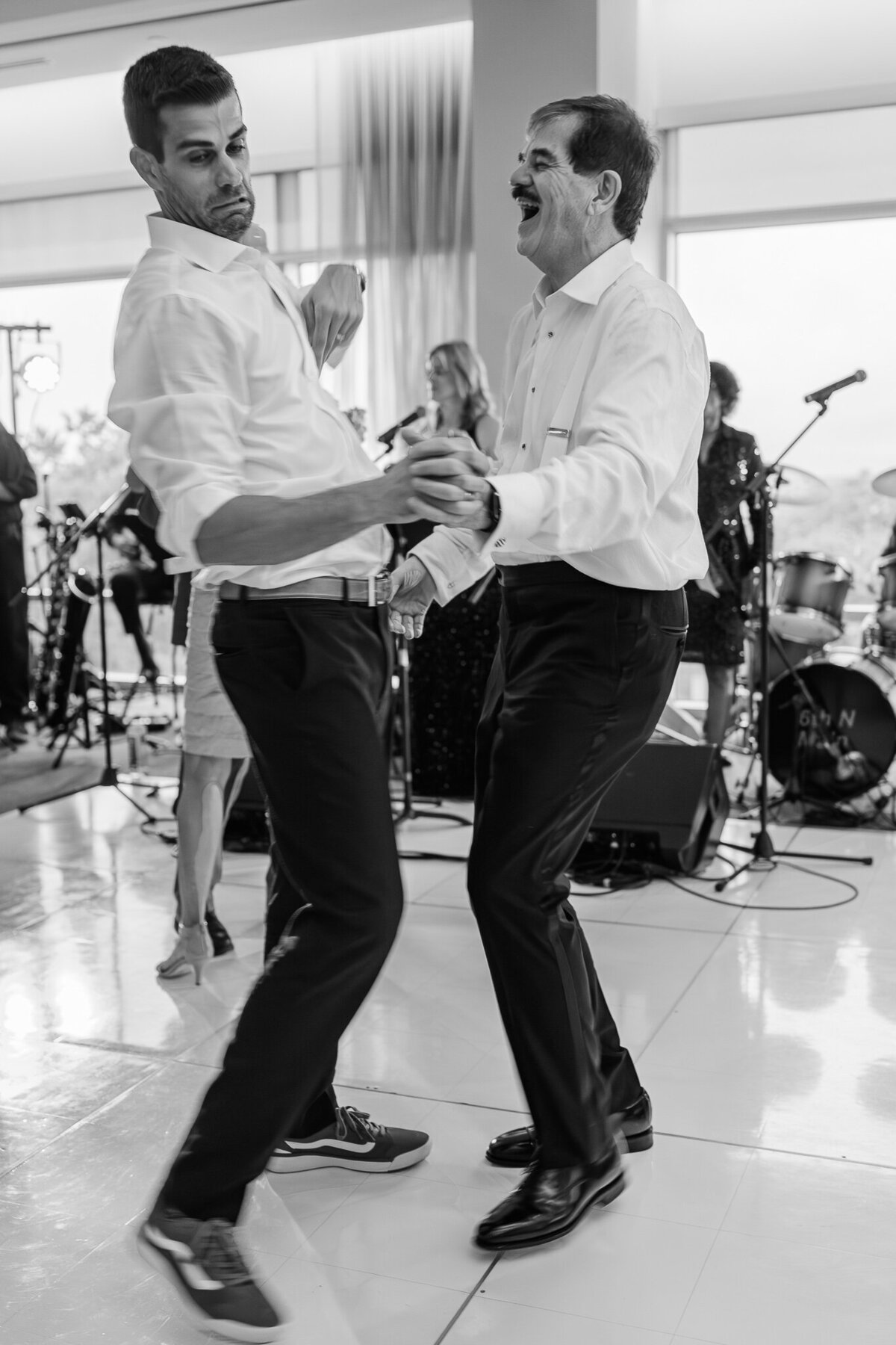 A groom and his brother dancing next to a live band enjoying their Wilmington wedding photography by JoLynn Photography