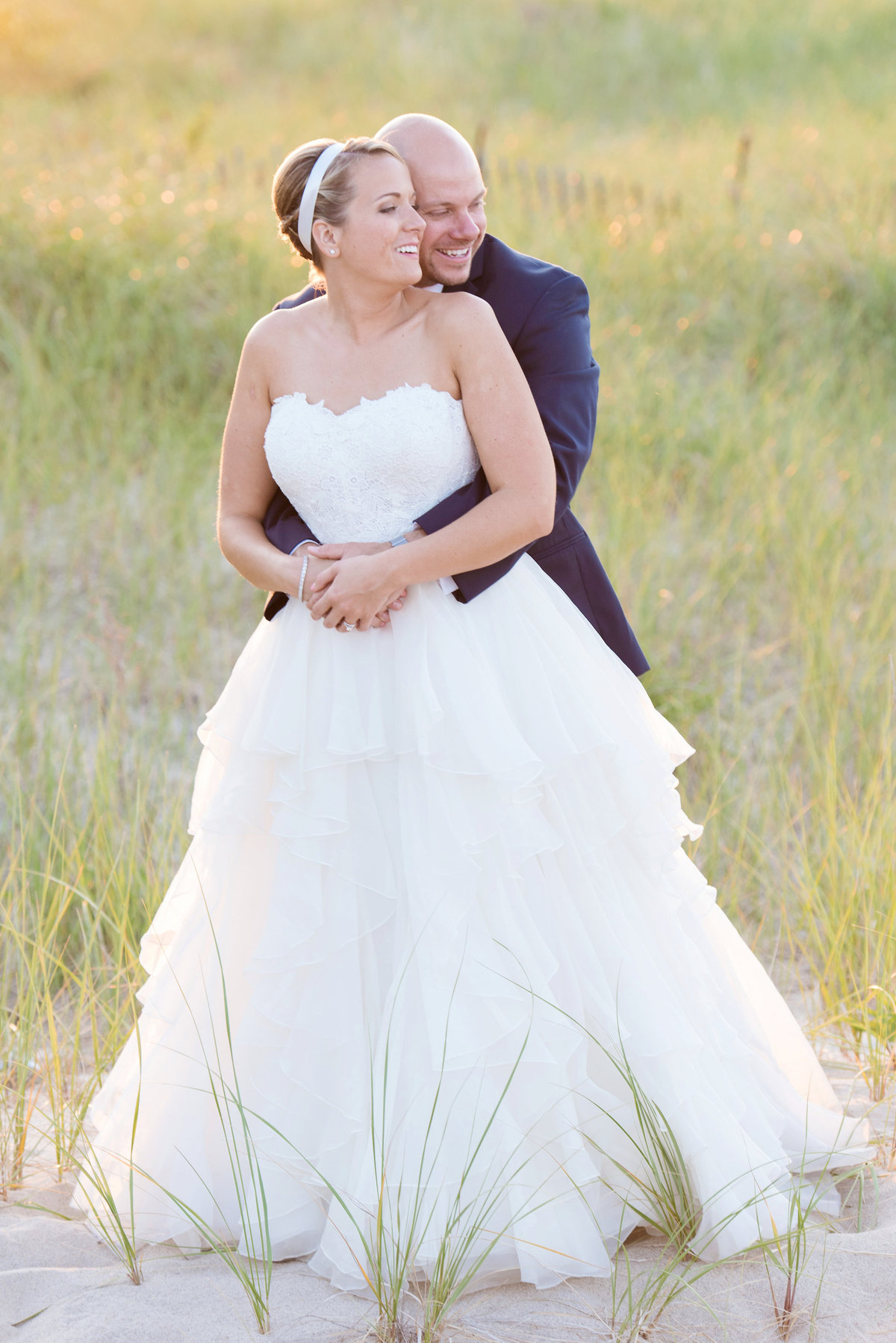groom hugging his bride from behind on the beach from wedding at Pavilion at Sunken Meadow