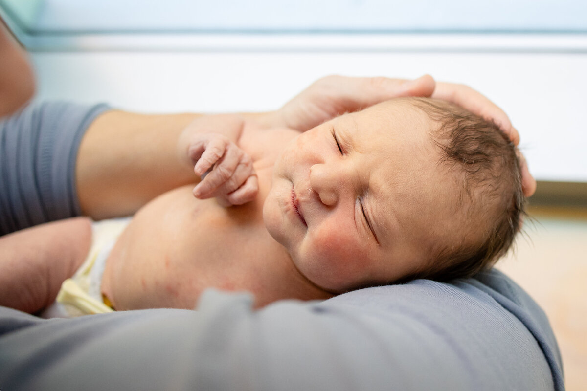 Newborn cradled in dad's arms by hospital room window