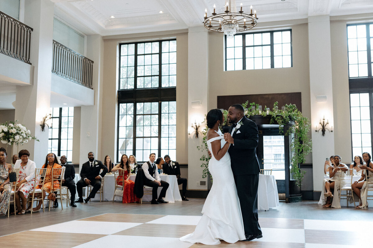 A bride and groom share their first dance at their reception at 1208 Washington Place in Columbia, SC. Greenery and their guests surround them at the tables.