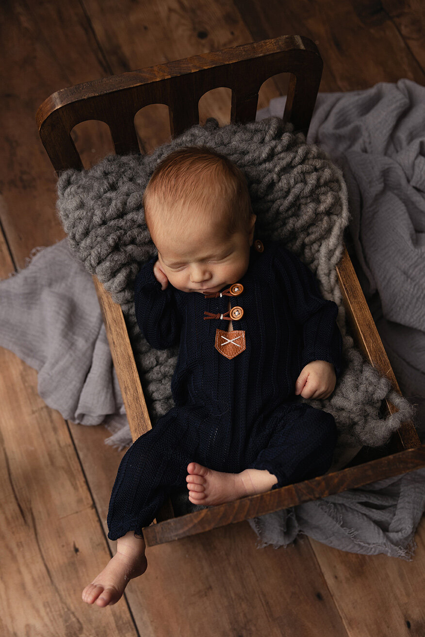 Baby sleeps in wooden bed with blue outfit and wooden buttons.