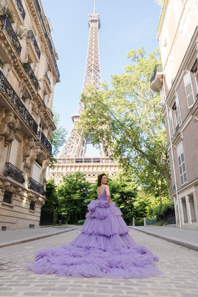 Paris portrait photography featuring woman in purple princess gown walking Parisian street with Eiffel Tower view