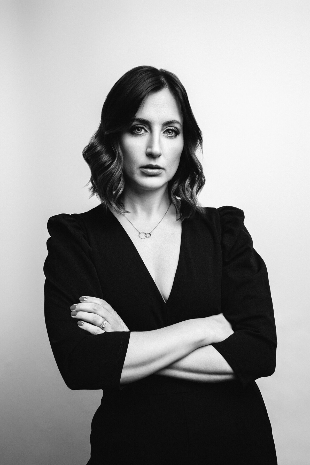 Black and White Portrait of woman wearing black jumpsuit with arms crossed.