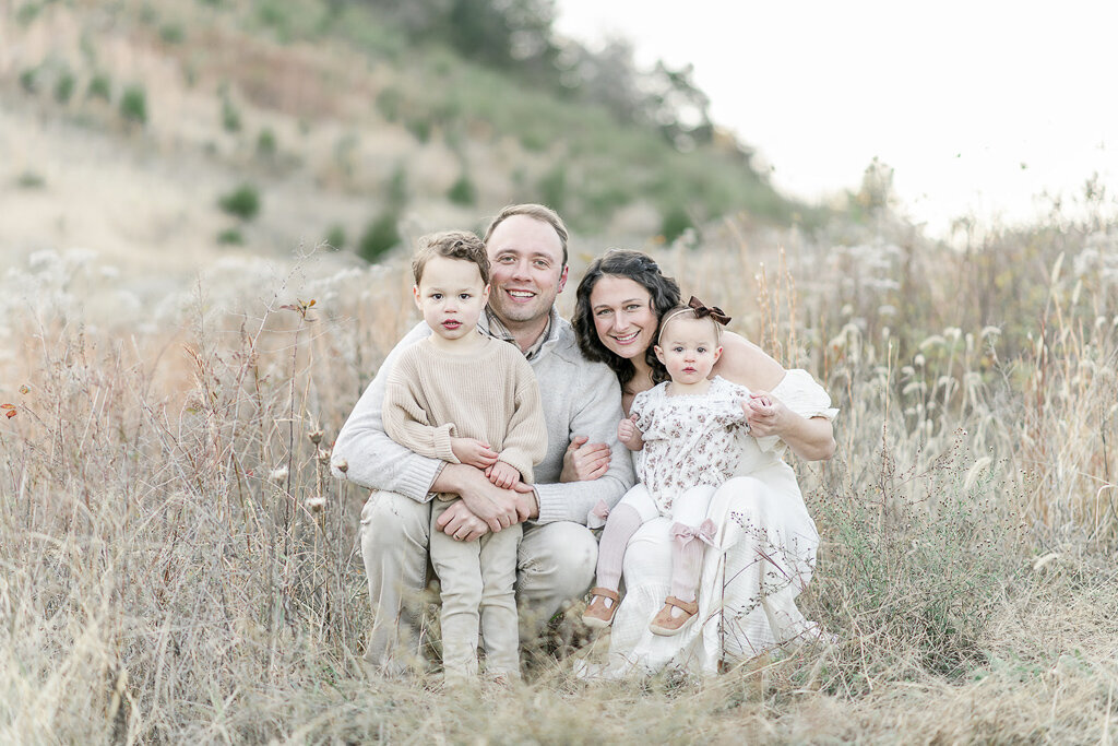 Family of 4 smiles as they sit in a field of golden grass