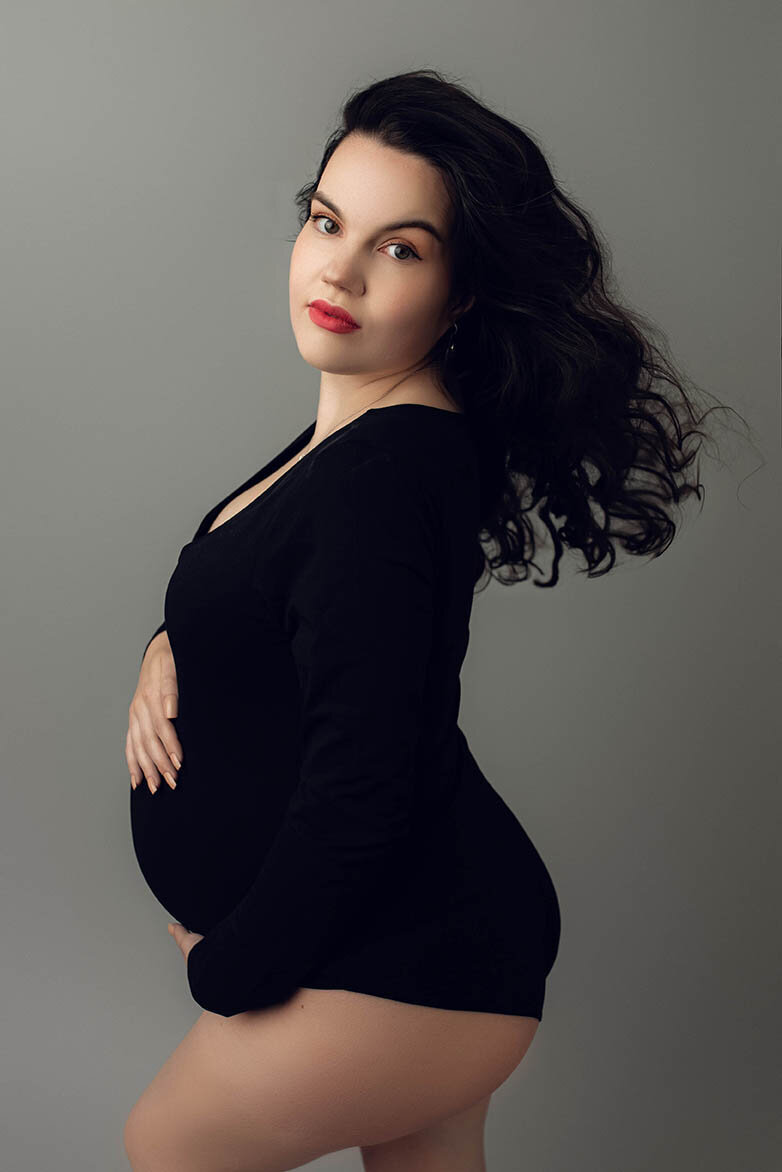 a pregnant woman holding her bump wearing a black bodysuit with  a fan blowing
