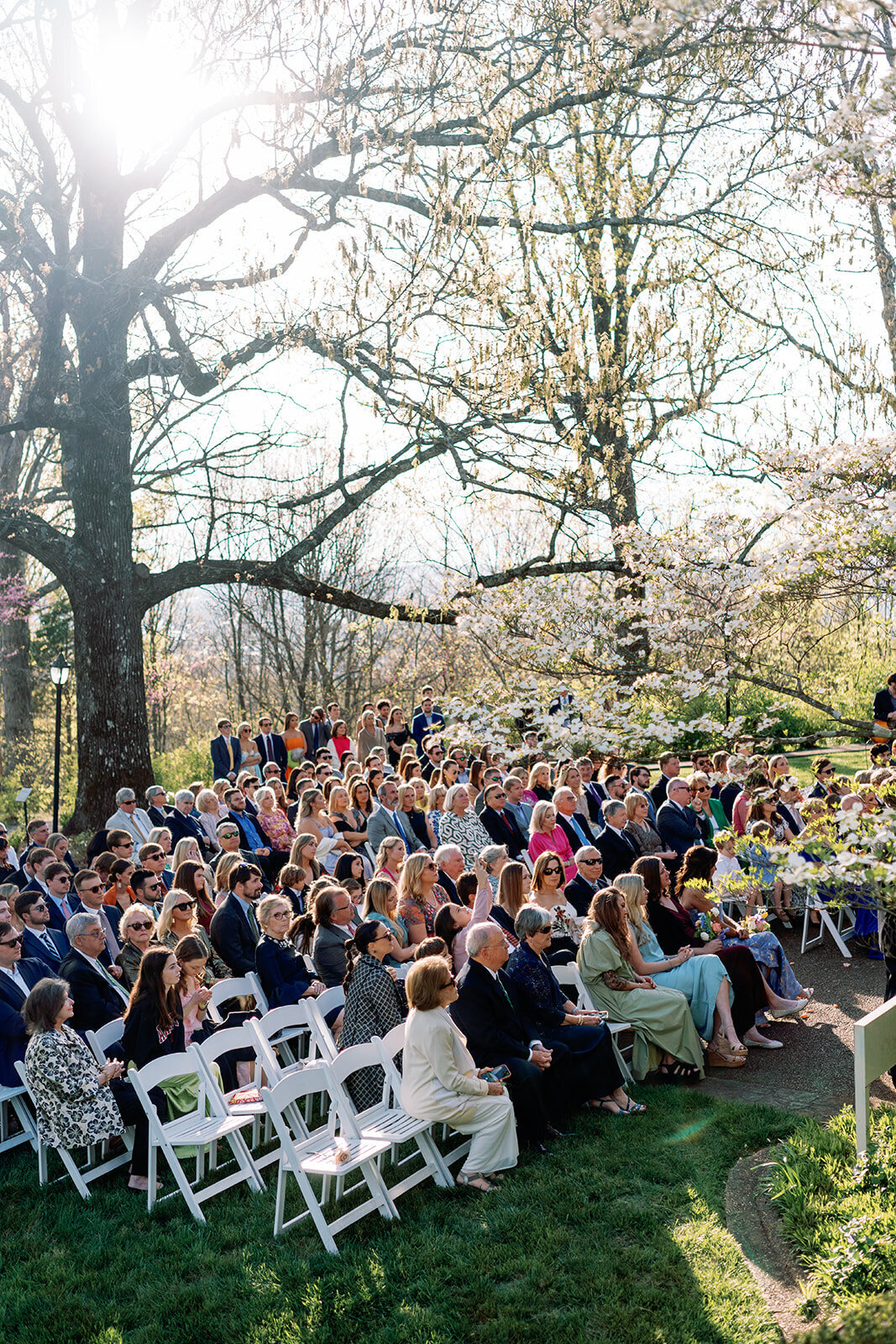 Guests seated outdoors beneath blooming spring trees, waiting for the wedding ceremony to begin at Burritt on the Mountain in Huntsville, Alabama, photographed by Perry Hancock.